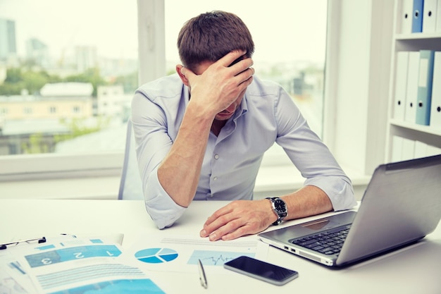 concept d'entreprise, de personnes, de paperasse et de délai - homme d'affaires stressé avec des papiers et des graphiques assis à table au bureau