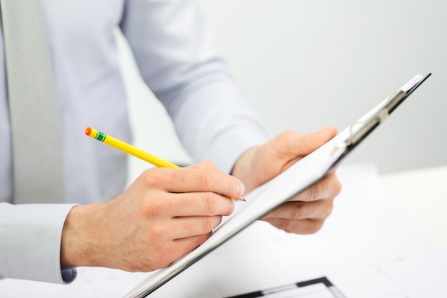 concept d'entreprise, de personnes et de paperasse - gros plan sur des mains d'homme d'affaires écrivant dans le presse-papiers au bureau