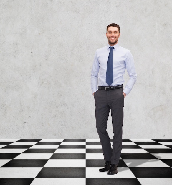 concept d'entreprise, de personnes et de stratégie - homme d'affaires souriant heureux en chemise et cravate sur un sol en damier sur fond gris