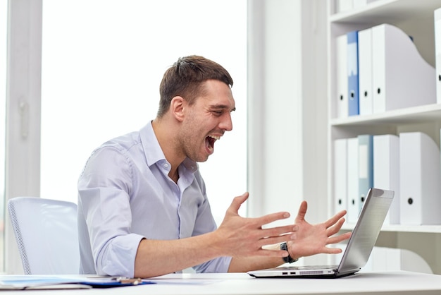 concept d'entreprise, de personnes, de stress, d'échec et de technologie - homme d'affaires en colère avec un ordinateur portable et des papiers criant au bureau