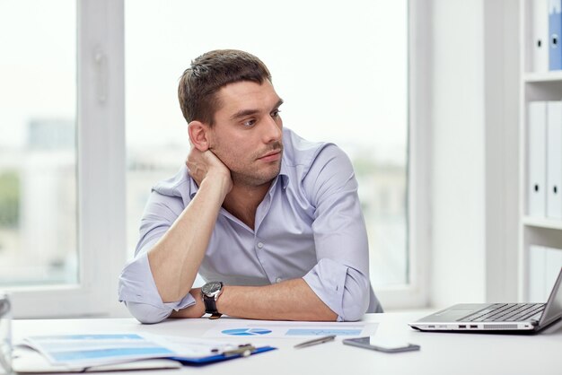 concept d'entreprise, de personnes et de technologie - homme d'affaires ennuyé avec ordinateur portable et papiers au bureau