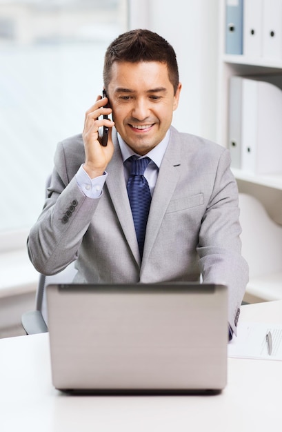 concept d'entreprise, de personnes et de technologie - homme d'affaires souriant avec ordinateur portable appelant sur smartphone au bureau