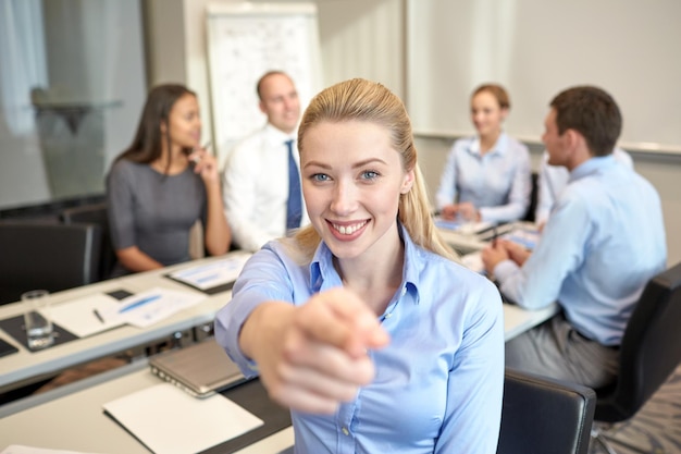 concept d'entreprise, de personnes et de travail d'équipe - femme d'affaires souriante pointant le doigt vers le haut avec un groupe d'hommes d'affaires réunis au bureau