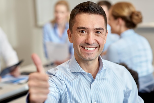 concept d'entreprise, de personnes et de travail d'équipe - homme d'affaires souriant montrant les pouces vers le haut avec un groupe d'hommes d'affaires réunis au bureau