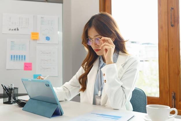 Concept d'entreprise réussi Femme d'affaires utilise la main pour tenir des lunettes tout en écrivant des données sur une tablette