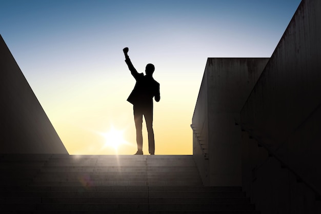 concept d'entreprise, de succès, de geste et de personnes - silhouette d'homme d'affaires heureux levant le poing et célébrant la victoire debout dans les escaliers sur fond clair du soleil