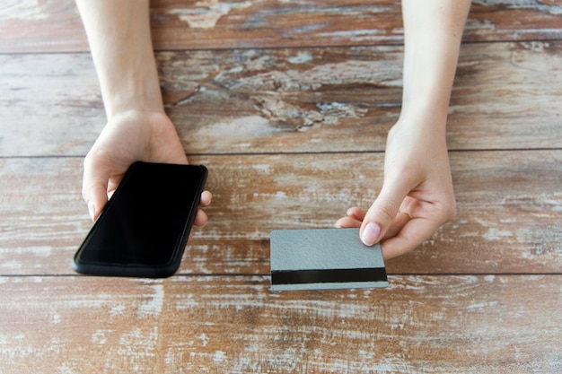 concept d'entreprise, de technologie, d'argent liquide et d'internet - gros plan de mains masculines tenant un smartphone et une carte de crédit sur une table en bois