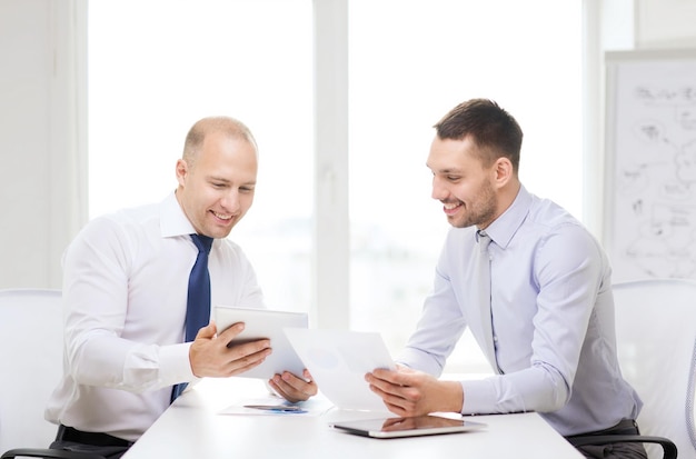 concept d'entreprise, de technologie et de bureau - deux hommes d'affaires souriants avec des ordinateurs tablettes et des fichiers au bureau