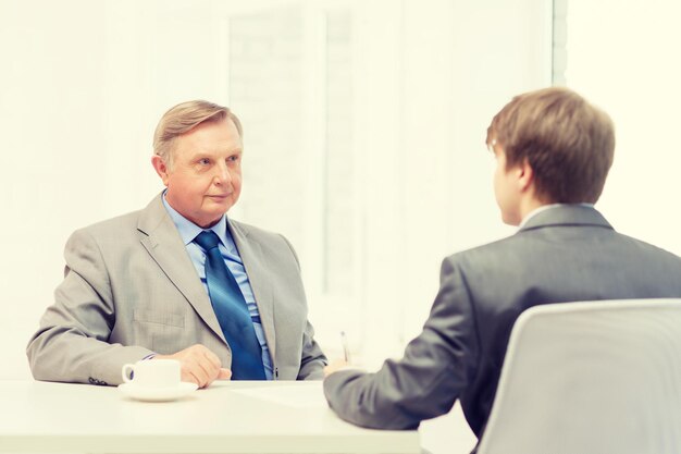 concept d'entreprise, de technologie et de bureau - homme plus âgé et jeune homme signant des papiers au bureau