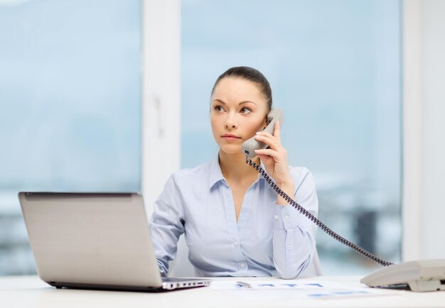 concept d'entreprise, de technologie et de communication - femme d'affaires souriante avec téléphone, ordinateur portable et fichiers au bureau