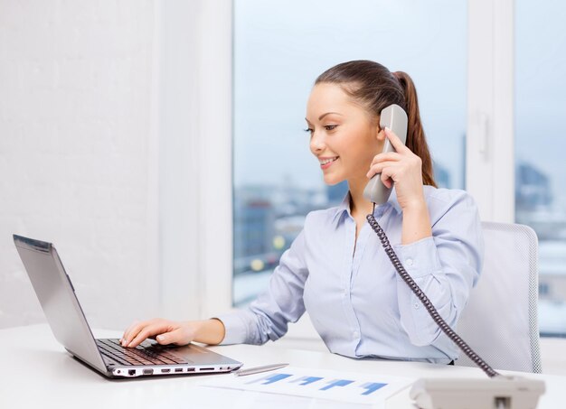 concept d'entreprise, de technologie et de communication - femme d'affaires souriante avec téléphone, ordinateur portable et fichiers au bureau