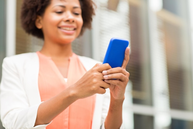 concept d'entreprise, de technologie, de communication et de personnes - gros plan d'une jeune femme d'affaires afro-américaine souriante envoyant des SMS sur un smartphone en ville