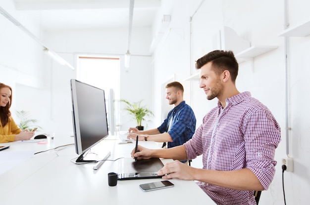 concept d'entreprise, de technologie, de design et de personnes - jeune homme créatif ou designer avec ordinateur et tablette à stylet travaillant au bureau