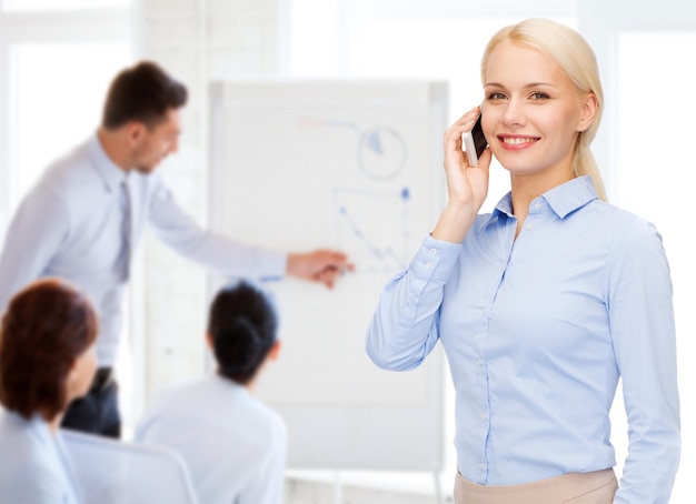 concept d'entreprise, de technologie, d'éducation et de personnes - jeune femme d'affaires souriante avec smartphone faisant appel au bureau