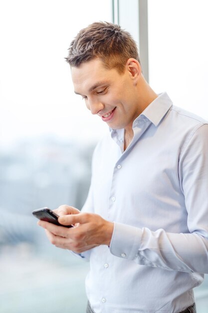 concept d'entreprise, de technologie, d'internet et de bureau - homme d'affaires souriant avec smartphone au bureau