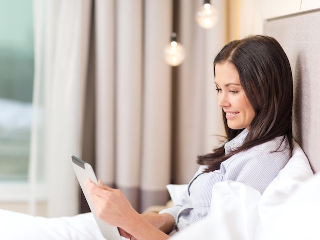 concept d'entreprise, de technologie, d'internet et d'hôtel - femme d'affaires heureuse avec ordinateur tablette couché dans l'hôtel au lit