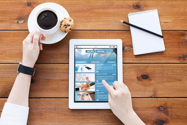 concept d'entreprise, de technologie, de médias de masse et de personnes - gros plan d'une femme avec des informations commerciales sur l'écran de l'ordinateur tablette, un ordinateur portable et un café sur une table en bois