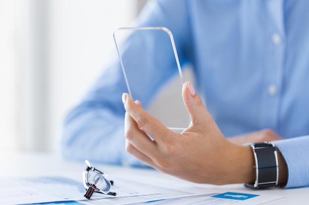 concept d'entreprise, de technologie et de personnes - gros plan sur une main de femme tenant et montrant un smartphone transparent au bureau