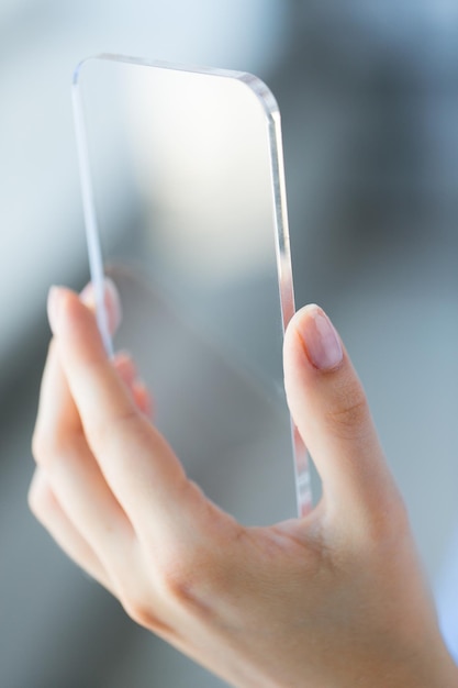 concept d'entreprise, de technologie et de personnes - gros plan sur une main de femme tenant et montrant un smartphone transparent au bureau