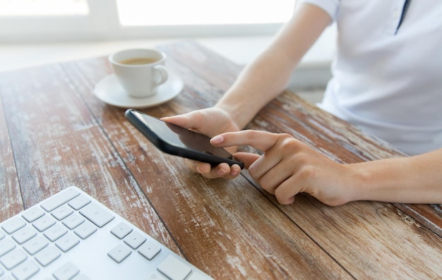 concept d'entreprise, de technologie et de personnes - gros plan d'une main masculine tenant un smartphone avec café et clavier à table en bois