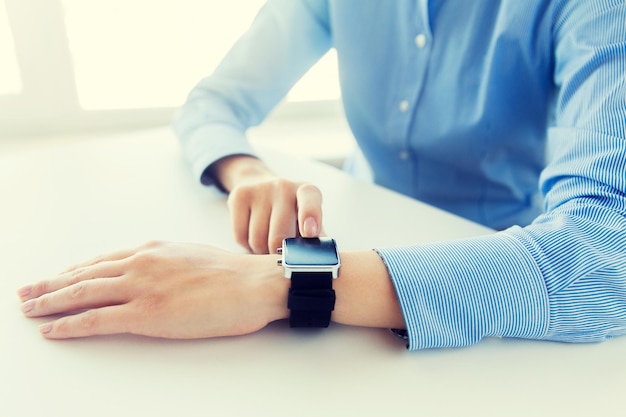 concept d'entreprise, de technologie et de personnes - gros plan sur des mains de femme définissant une montre intelligente au bureau