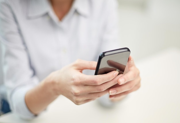 concept d'entreprise, de technologie et de personnes - gros plan sur des mains de femme envoyant un message texte sur un smartphone au bureau