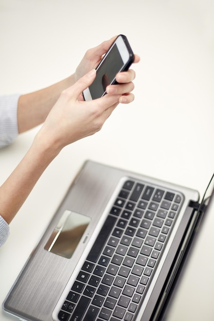 concept d'entreprise, de technologie et de personnes - gros plan sur les mains d'une femme avec un ordinateur portable et un message SMS sur smartphone au bureau