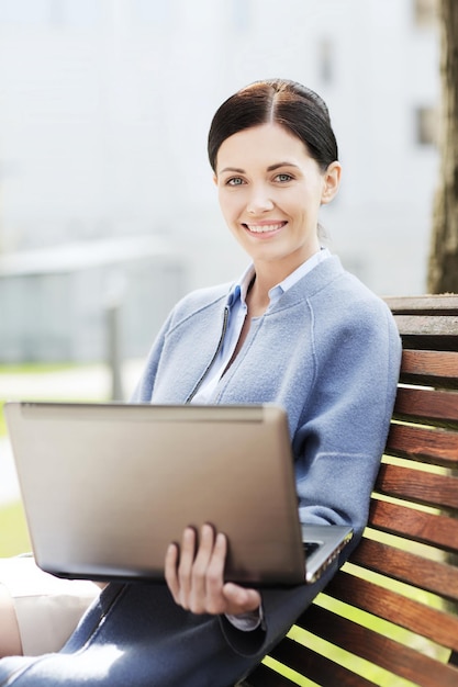 concept d'entreprise, de technologie et de personnes - jeune femme souriante avec un ordinateur portable assis sur un banc en ville