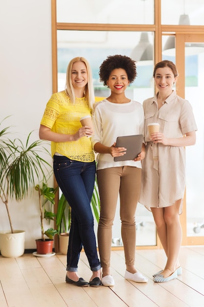 concept d'entreprise, de technologie, de personnes et de travail d'équipe - équipe créative internationale heureuse de trois femmes avec ordinateur tablette et café au bureau