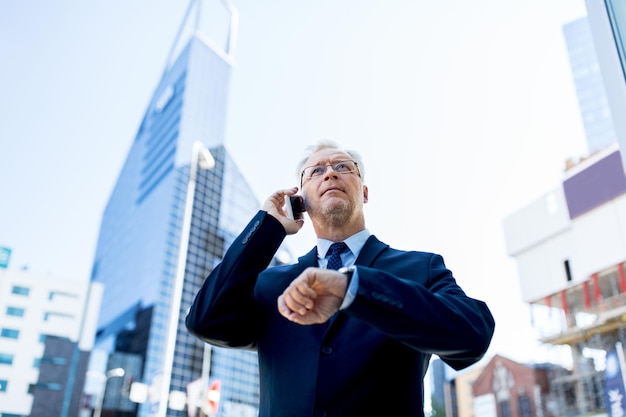 concept d'entreprise, de technologie, de temps, de ponctualité et de personnes - homme d'affaires senior appelant sur smartphone avec montre-bracelet ou montre intelligente à la main en ville