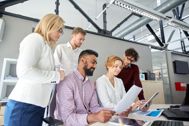 concept d'entreprise, de travail d'équipe et de personnes - équipe créative internationale avec des papiers et des ordinateurs tablettes au bureau