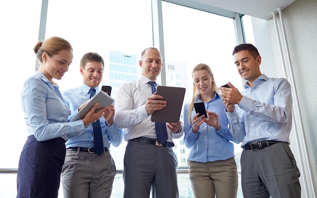 concept d'entreprise, de travail d'équipe, de personnes et de technologie - équipe commerciale avec tablette pc et smartphones se réunissant au bureau