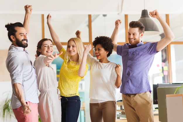 concept d'entreprise, de triomphe, de geste, de personnes et de travail d'équipe - joyeuse équipe créative internationale levant les mains et célébrant la victoire au bureau