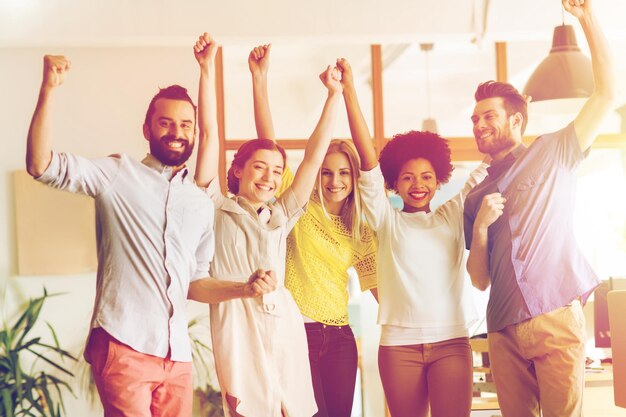 Photo concept d'entreprise, de triomphe, de geste, de personnes et de travail d'équipe - joyeuse équipe créative internationale levant les mains et célébrant la victoire au bureau