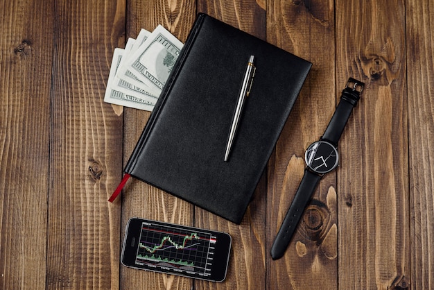 Concept d'entreprise - vue de dessus du téléphone avec graphique financier à l'écran, montre, stylo, ordinateur portable et argent
