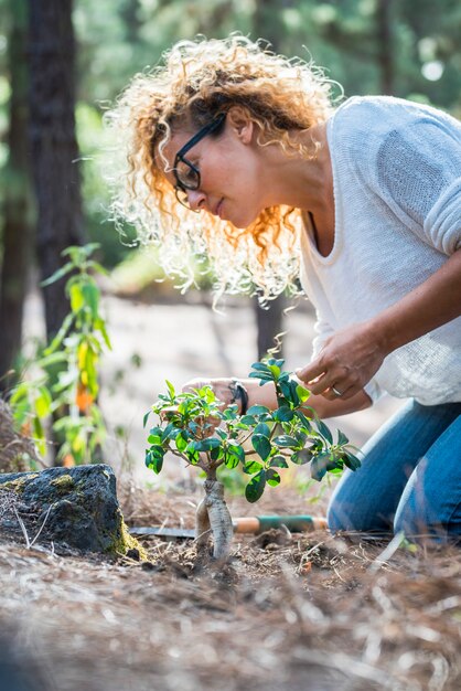 Concept d'environnement avec une belle jeune femme adulte bouclée s'occuper de nouvelles plantes dans la forêt