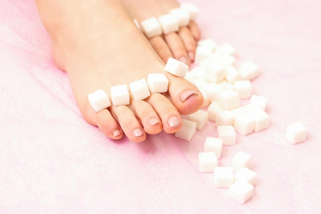 Le concept d'épilation à la cire Cubes de sucre allongés dans une rangée sur les orteils des pieds féminins sur fond rose