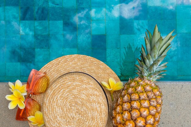 Photo concept d'été chapeau lunettes fleurs d'ananas au bord de la piscine