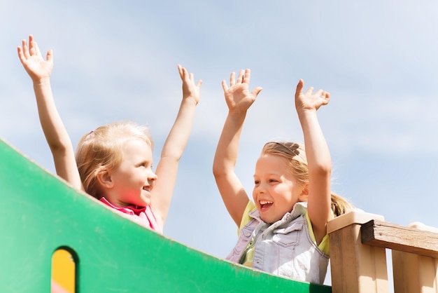concept d'été, d'enfance, de loisirs, d'amitié et de personnes - petites filles heureuses agitant les mains sur le cadre d'escalade de l'aire de jeux pour enfants