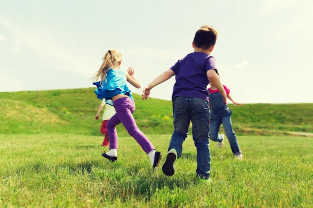 concept d'été, d'enfance, de loisirs et de personnes - groupe d'enfants heureux jouant au jeu de balises et courant sur un terrain vert à l'extérieur