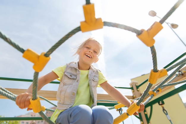 concept d'été, d'enfance, de loisirs et de personnes - petite fille heureuse sur le cadre d'escalade de l'aire de jeux pour enfants