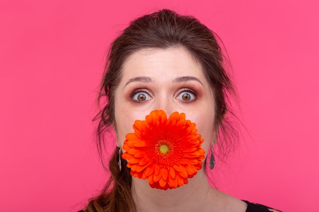 Photo concept d'été, de fleurs, de drôle et de personnes - femme s'amusant avec des gerberas sur la surface rose