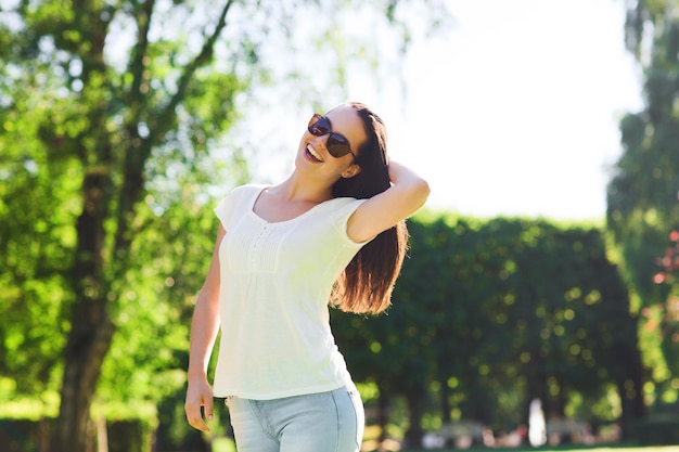 concept d'été, de loisirs, de vacances et de personnes - jeune femme souriante portant des lunettes de soleil debout dans le parc