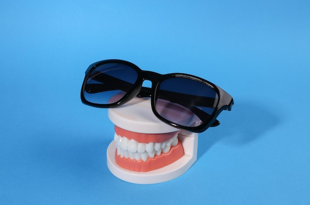 Concept d'été minimal Modèle en plastique d'une mâchoire humaine avec des lunettes de soleil sur fond bleu