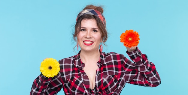 Concept d'été, de pin-up et d'amusement - jolie femme avec des gerberas sur fond bleu