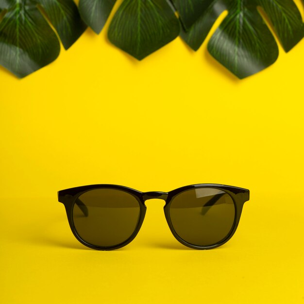 Concept d'été et de vacances. Lunettes de soleil et feuilles tropicales sur fond de couleur jaune