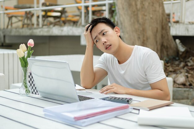 Concept d'étude en ligne le jeune étudiant en ligne regarde son ordinateur portable avec la main sur la tête, l'air stressé et anxieux à propos de la note de l'examen.