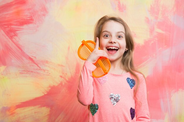 Concept Eurêka. Une fille heureuse a une idée sur un mur abstrait coloré. Modèle bébé avec des lunettes de soleil orange dans des vêtements à la mode. Mode enfant