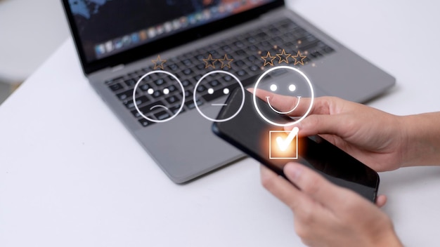 Le concept d'évaluation du service client à l'aide d'un smartphone appuie sur l'émoticône du visage souriant de satisfaction sur l'écran tactile virtuel