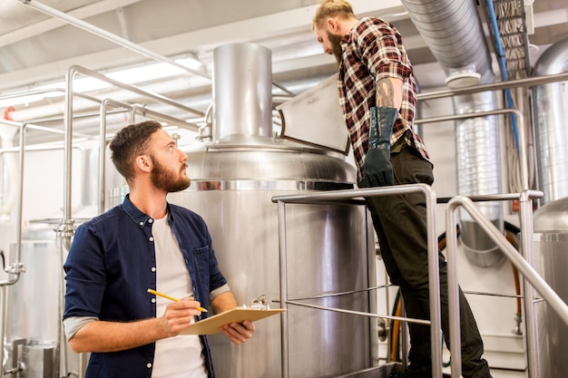 concept de fabrication, d'affaires et de personnes - hommes avec un bloc-notes travaillant dans une brasserie artisanale ou une usine de bière